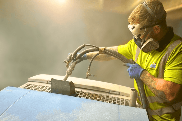 Jamie sandblasting machinery whilst wearing high vis clothing whilst wearing goggles and breathing mask.