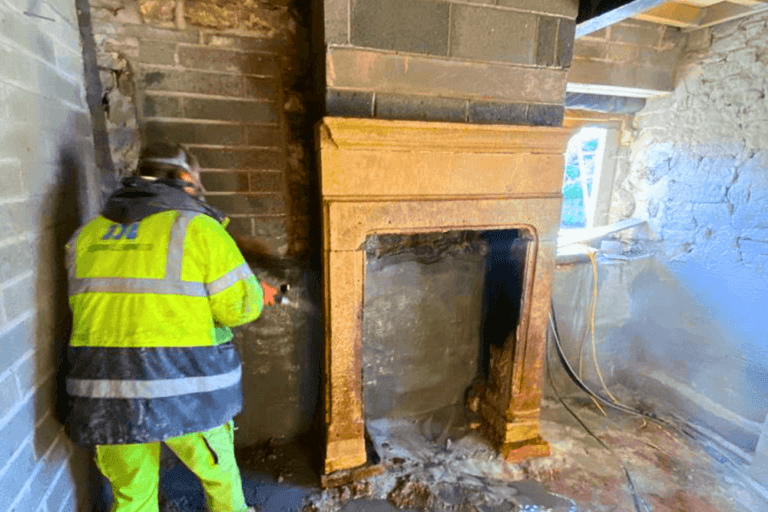 Worker media blasting fireplace inside residential property.